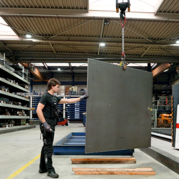 Steel plate suspended vertically from an overhead crane using a plate lifting clamp, with an operator guiding it